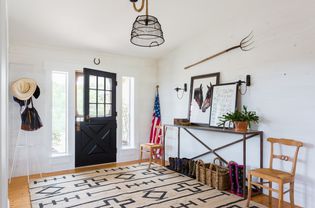A white entryway is decorated with Western style decor items that include a framed horse picture and a pitchfork hung parallel to the floor but above a small side table.
