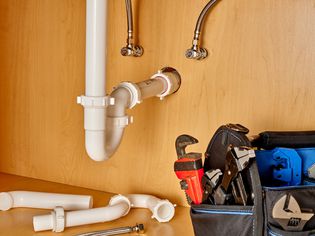 Drain pipes and water supply tubes next to plumbing tools and materials under sink