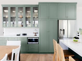 Kitchen with sage green-like painted cabinets with white marble tops and stainless steel appliances