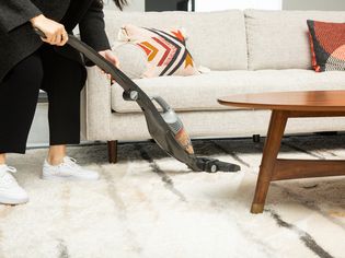 Person using BLACK+DECKER HSVB420J POWERSERIES 2-in-1 Cordless Stick Vacuum to clean carpet under couch