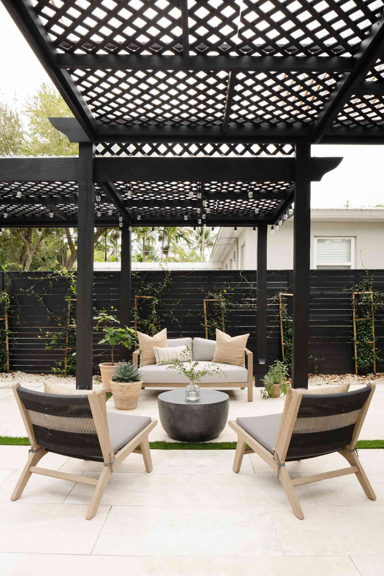 Black pergola and fence with a white house behind it