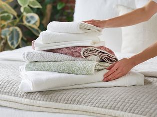 Hands placing sheets and towels on top of a bed