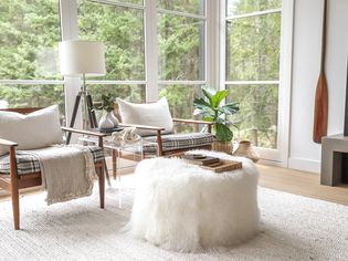 Small living room with wall to ceiling windows, two chairs and a coffee table with white fur covering