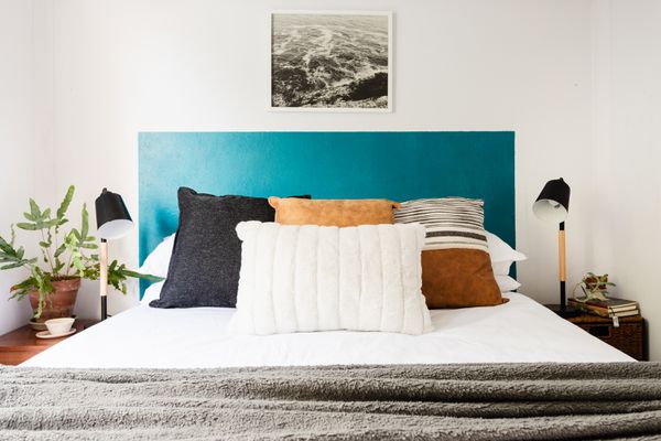 Teal blue DIY headboard behind bed with white, brown and black pillows