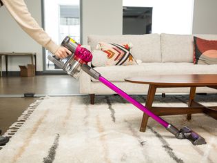 A person using the Dyson v7 Motorhead Cordless Stick Vacuum Cleaner to clean a rug