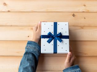 Person holding a white gift box wrapped with blue ribbon
