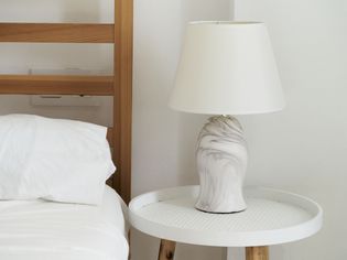 Marble table lamp with white shade on nightstand next to wooden bed with white bedding