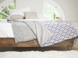 Reversible weighted blanket on a wood frame bed with white sheets on it