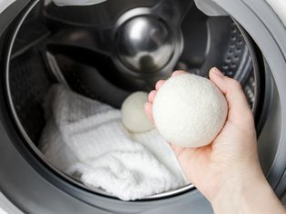 Person placing a white wool dryer ball inside dryer