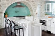 White kitchen with marble countertops, stone arch, and a bi-level countertop