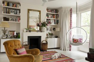 Living room with a bay window, built-in bookshelves, an Aztec-style rug, a yellow velvet armchair, and a lounging white dog.