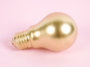 Gold-painted light bulb on a pink surface