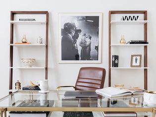 Home office with leaning wooden and white book shelves with glass desk and brown leather chair