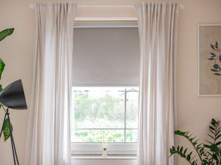 Cream-colored curtains hung on either side of window with gray blinds