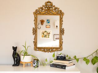 Gold ornate mirror hanging on wall above dresser top with decor and plants