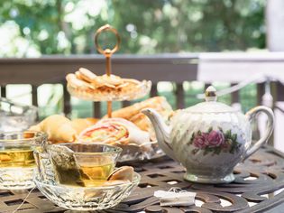 Decorative porcelain teapot and glass teacups next to pastries for afternoon tea party