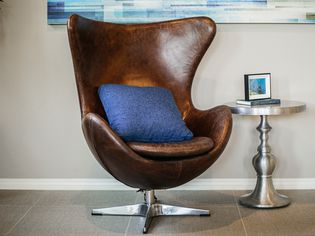 Brown leather Arne Jacobsen egg chair with blue throw pillow