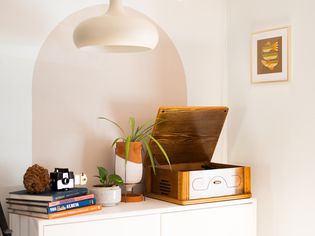 Tan-colored painted arch behind console table with record player, houseplant and books