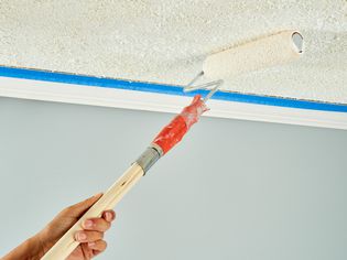 A peron rolling paint onto a popcorn texture ceiling.