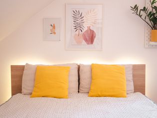 Made bed with yellow throw pillows surrounded by ambient light