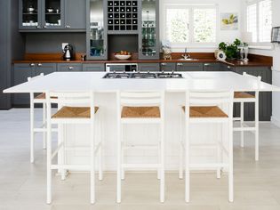 White kitchen island with matching white chairs in front of gray kitchen cabinets