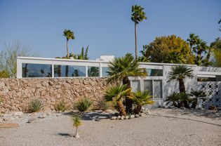 White modern home in desert landscaping and palms in front