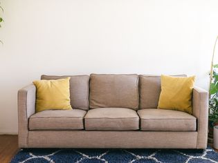 Tan couch with yellow cushions next to houseplants and blue rug