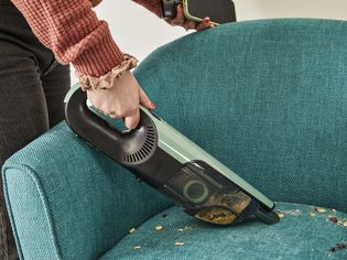 Person using Shark UltraCyclone Pro Cordless Handheld Vacuum to clean food from blue chair