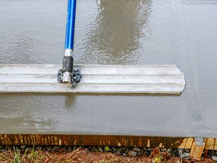A person using a bull float to smooth a wet concrete slab.