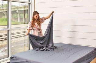 Woman adding Bampure Sheets to a bed with a wooden frame