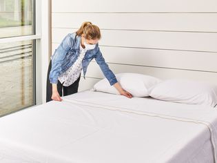 Person wearing mask making bed with Kassatex Salerno Percale Sheet Set