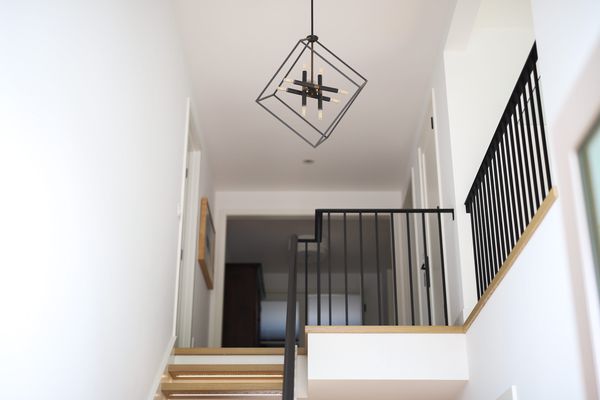 Foyer chandelier with geometric designs over black railing near staircase