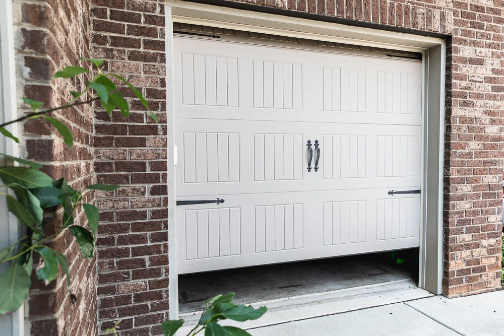 White garage door partially opened surrounded by brick walls and branches