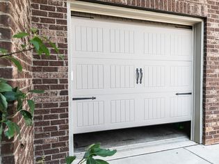 White garage door partially opened surrounded by brick walls and branches