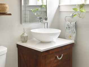 White vessel sink with wooden cabinet next to hanging towel and houseplant