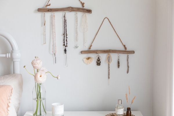 Jewelry hanging from driftwood with hooks over nightstand with decor items closeup