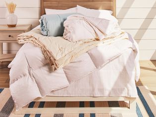 Multiple down comforters sitting on bed with a wooden headboard 