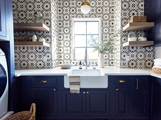 A navy blue laundry room with patterned wallpaper and floating shelves.