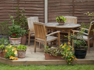 Wooden table, chairs and fruit and vegetables in plant pots on patio decking in garden